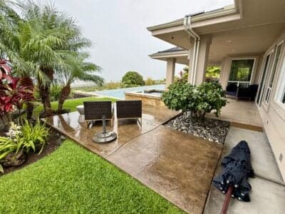 Rain-soaked patio in Kailua-Kona, Hawaii, featuring lush greenery, modern outdoor furniture, and an umbrella, illustrating the impact of Kona storms on local weather conditions.