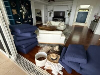 Outdoor cushions stacked indoors with a sun hat and bucket, illustrating preparation for a Kona storm in a modern Hawaiian home.