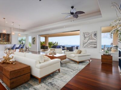 Interior living area where wide pocket doors retract into the walls to create a continuous indoor-outdoor transition. Hardwood flooring extends to the threshold of the covered lanai, allowing unobstructed airflow and ocean views.