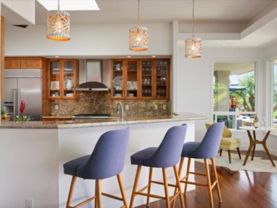 Kitchen workspace featuring polished granite countertops, raised bar seating with upholstered stools, and pendant lighting overhead. Custom wood cabinetry with glass-front upper cabinets provides storage and display space.
