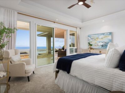 Primary bedroom with high ceilings and large sliding glass doors leading toward outdoor areas. Natural light enters from multiple openings framing views of the ocean and landscape.