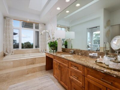 Ocean view bathroom featuring a tub, extended granite countertop and wood cabinetry base. Large mirror panels and overhead lighting.